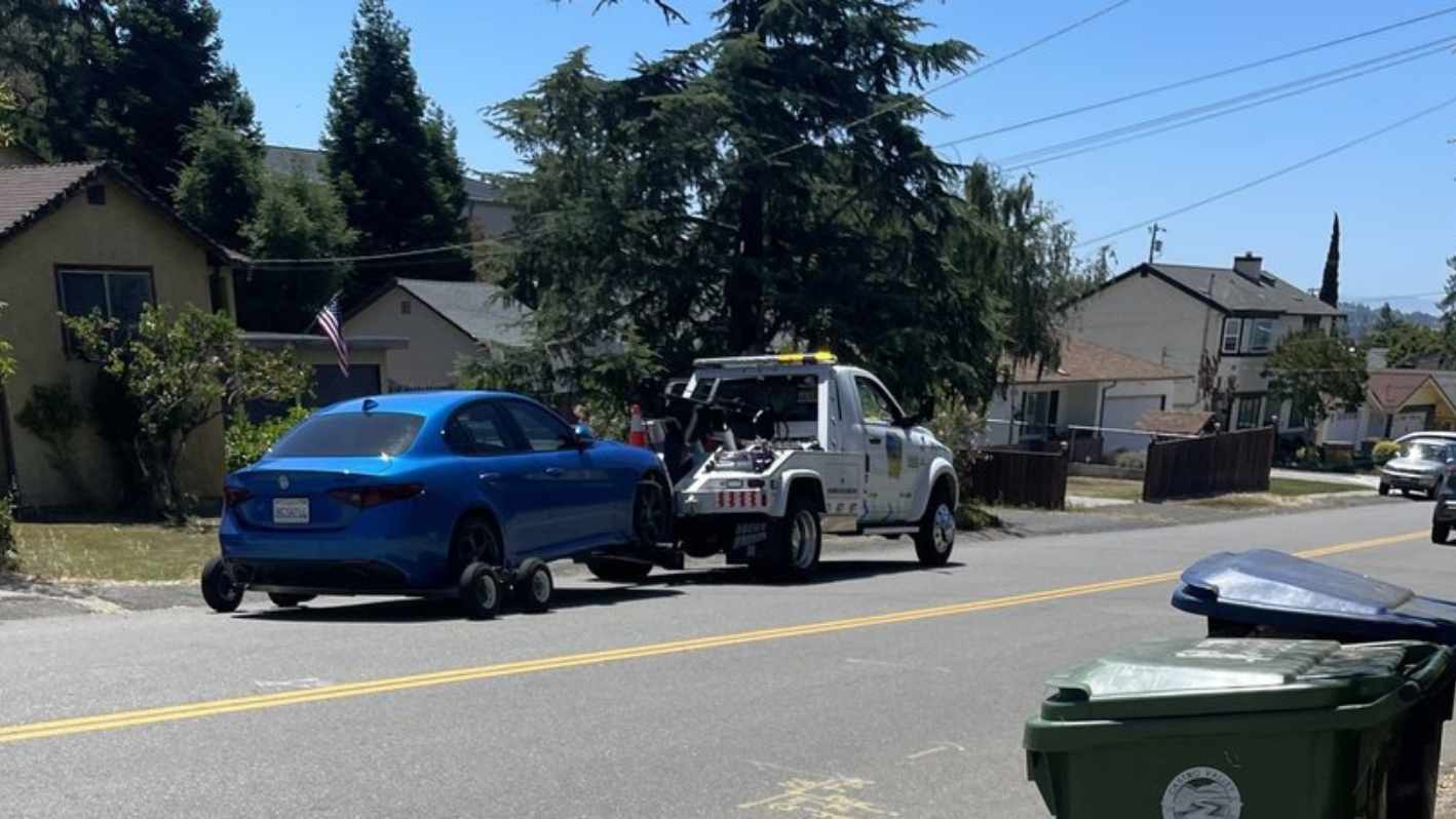 A tow truck towing a blue car down a street